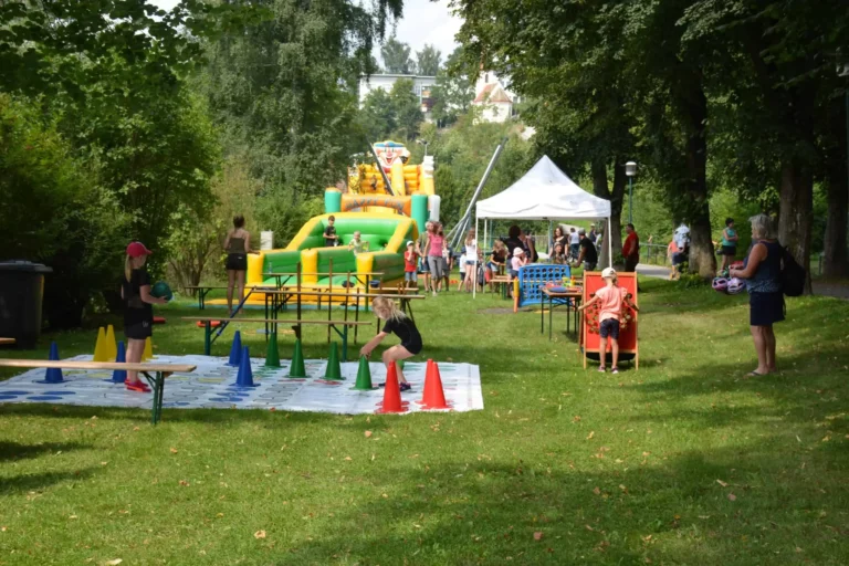 Auf dem Rasenplatz spielen Kinder Spiele, darunter eine Hüpfburg und Twister.