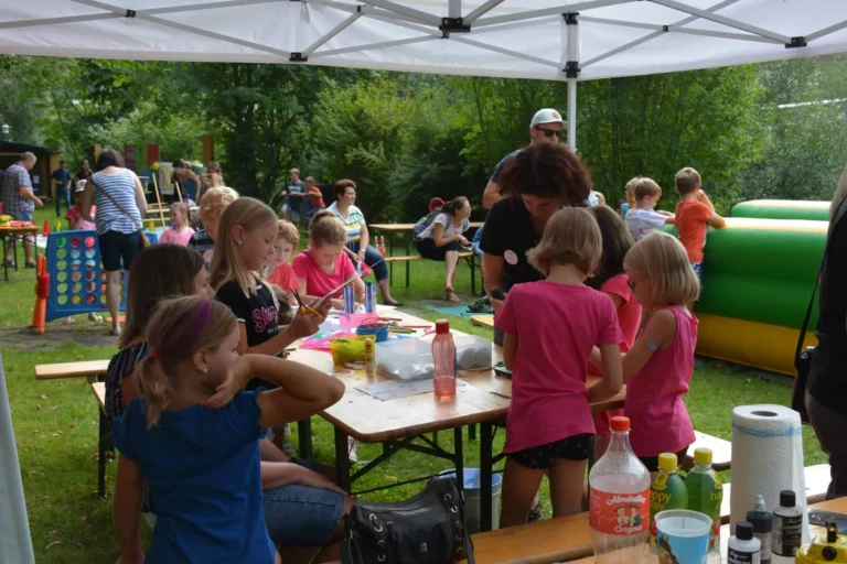 Kinder basteln an Tischen unter einem Zelt bei einer Veranstaltung im Freien.