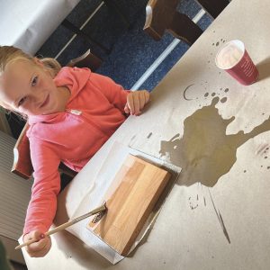 Ein Mädchen ölt ein Holzbrett mit einem Pinsel, Farbe verschüttet.