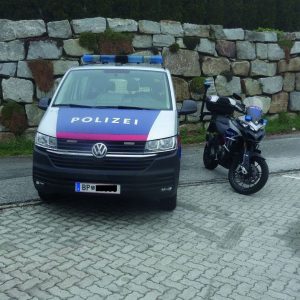 Ein Polizeiwagen und ein Motorrad stehen vor einer Steinmauer.
