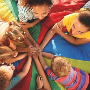 Sechs Kinder und zwei Erwachsene liegen im Kreis auf einer bunten Matte und legen ihre Hände in der Mitte zusammen.